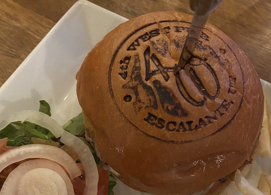 A burger with a 4th West Pub Escalante Utah logo branded into the bun, served with a side salad