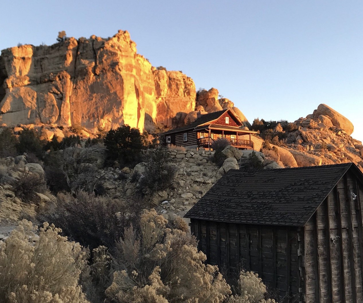 A wooden cabin glowing at sunset beneath tall sandstone cliffs near Boulder Utah