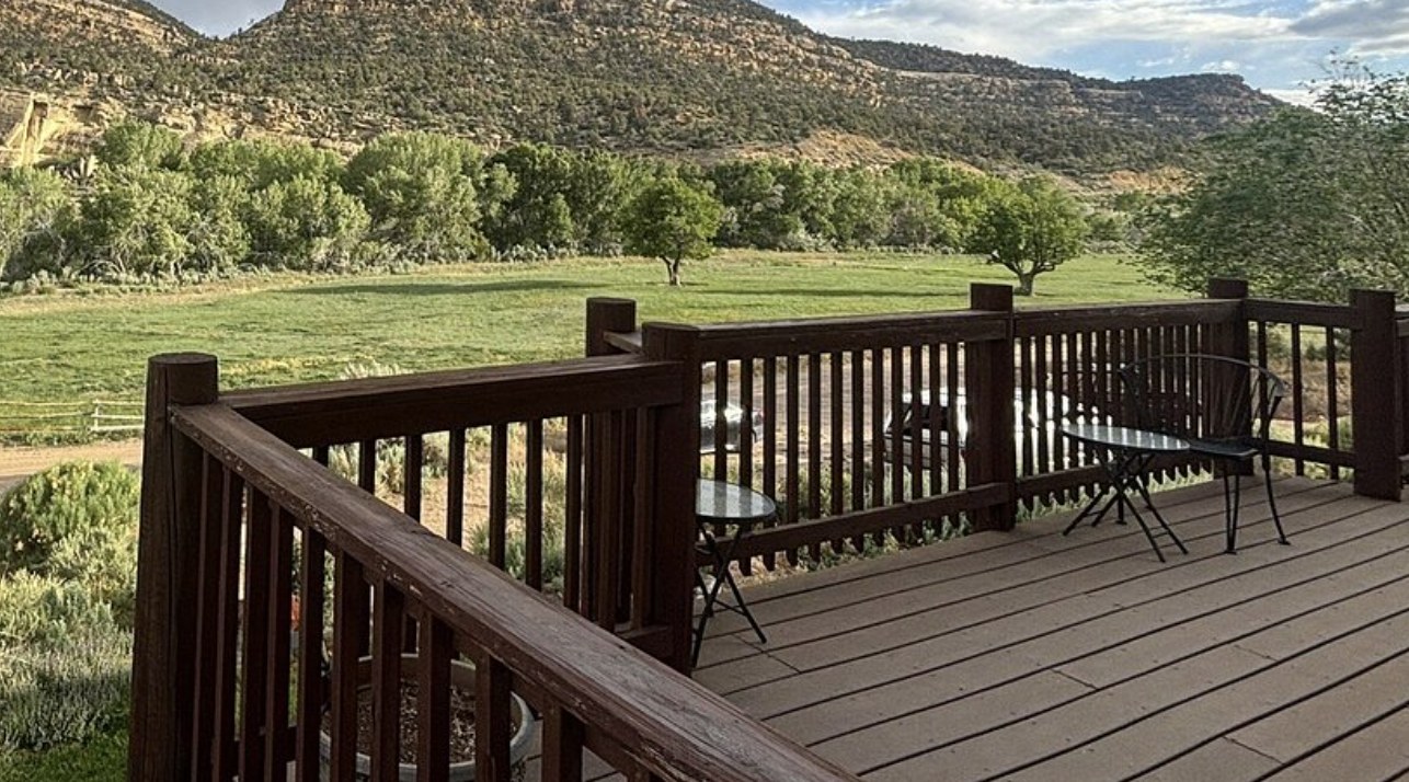 A wooden deck with patio chairs overlooking a green pasture and cliffs near Boulder Utah