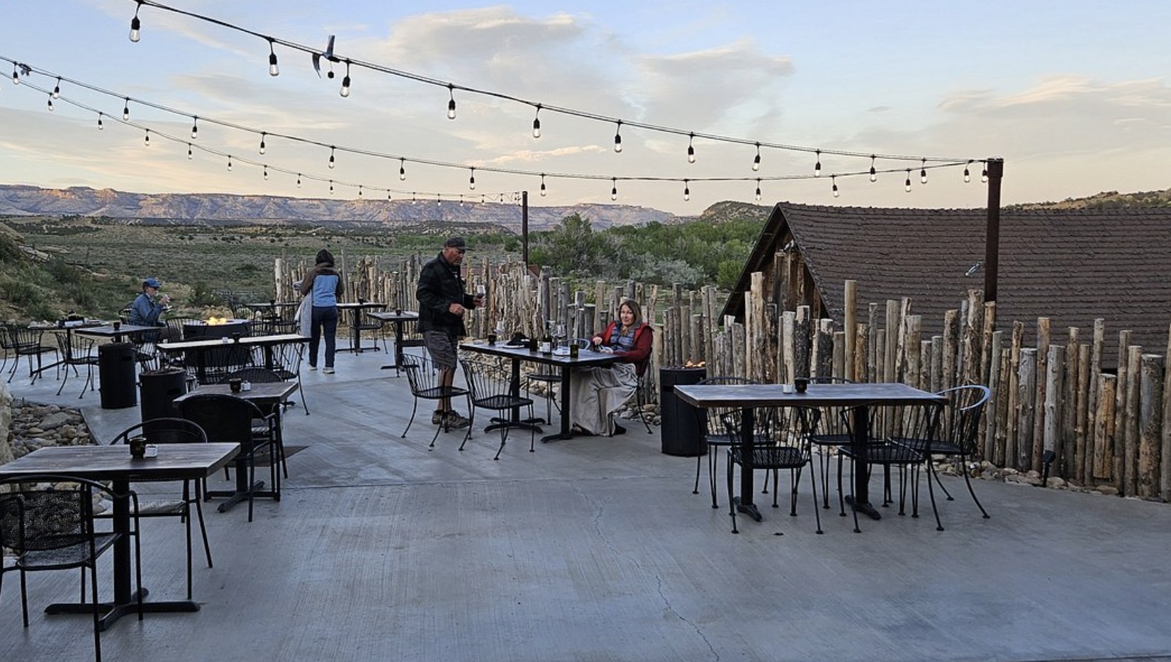 Guests dining at an outdoor patio with string lights and a log post fence at dusk near Boulder Utah