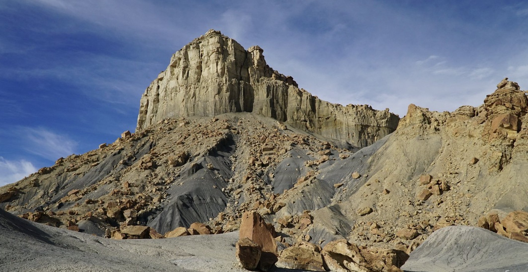 A sandstone butte rising above grey badlands hills along the Burr Trail area