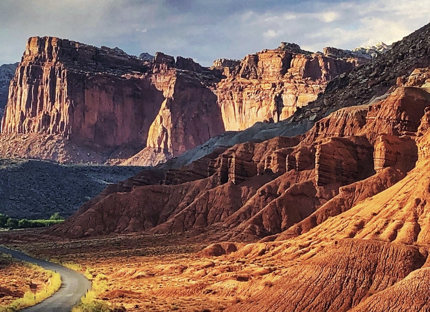 A paved road winding below tall red cliffs along the Burr Trail