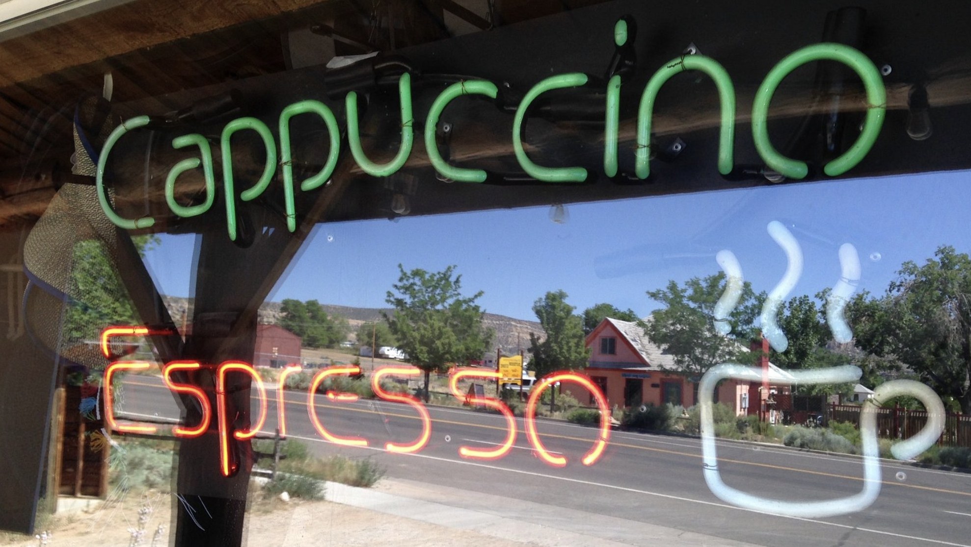 A neon Cappuccino and Espresso sign in a cafe window with Main Street reflected in the glass in Escalante