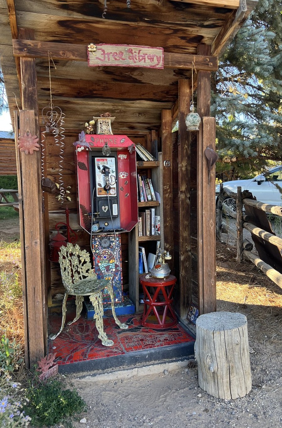 A converted phone booth turned into a small free library with books and a mosaic tile floor in Escalante