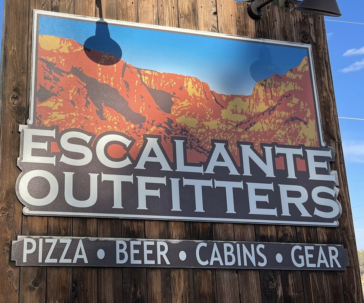 Close up of the Escalante Outfitters sign listing pizza, beer, cabins, and gear